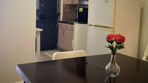 A compact kitchen with a refrigerator, microwave, and wooden cabinets. A dining table with a vase of flowers is in the foreground. - Historic Ocean Park Near Beach Water Reserve Fiber Internet Fast WiFi (San Juan)