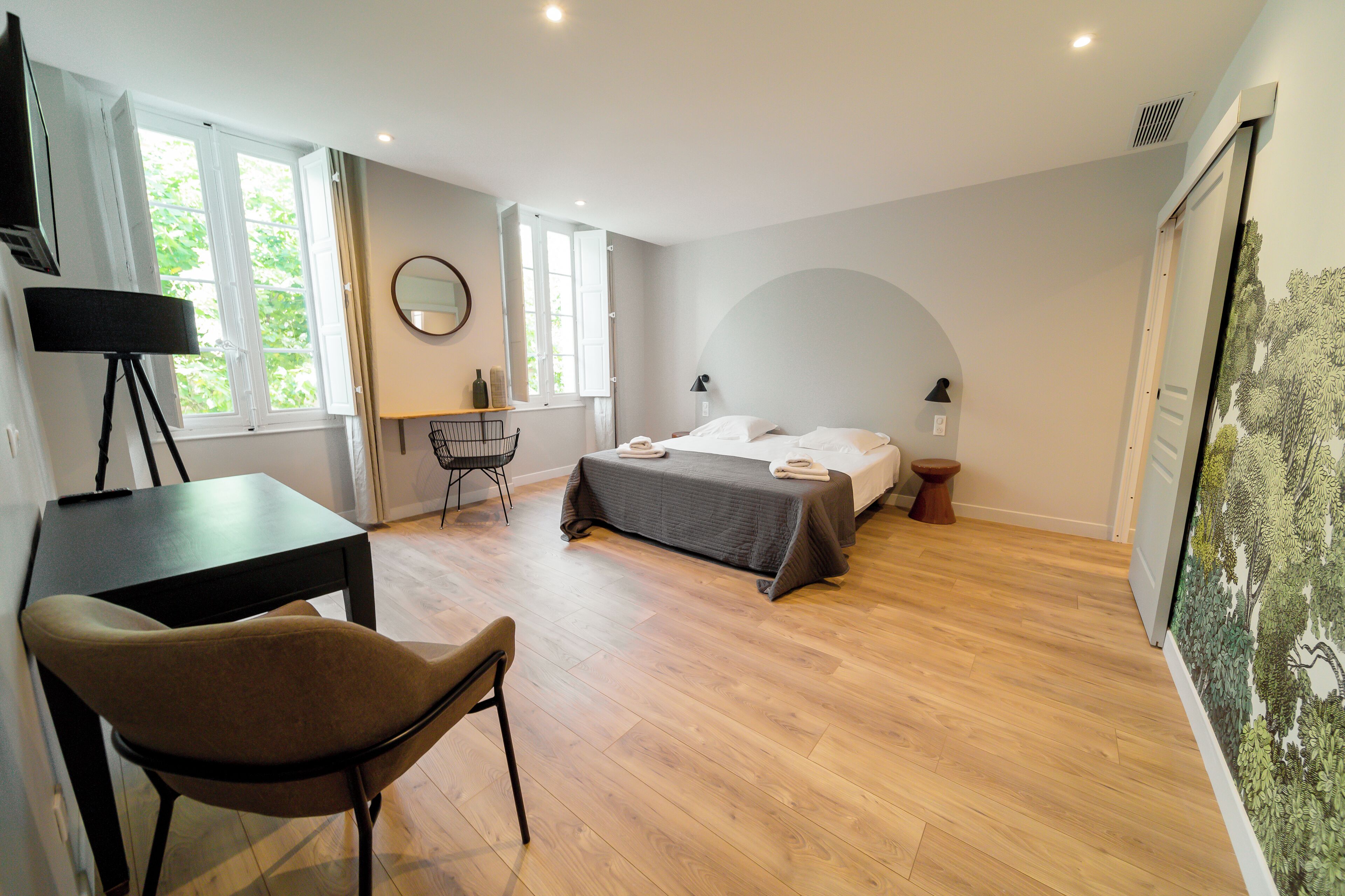 A bedroom with a bed, bedside tables, a desk, a chair, and a large window.