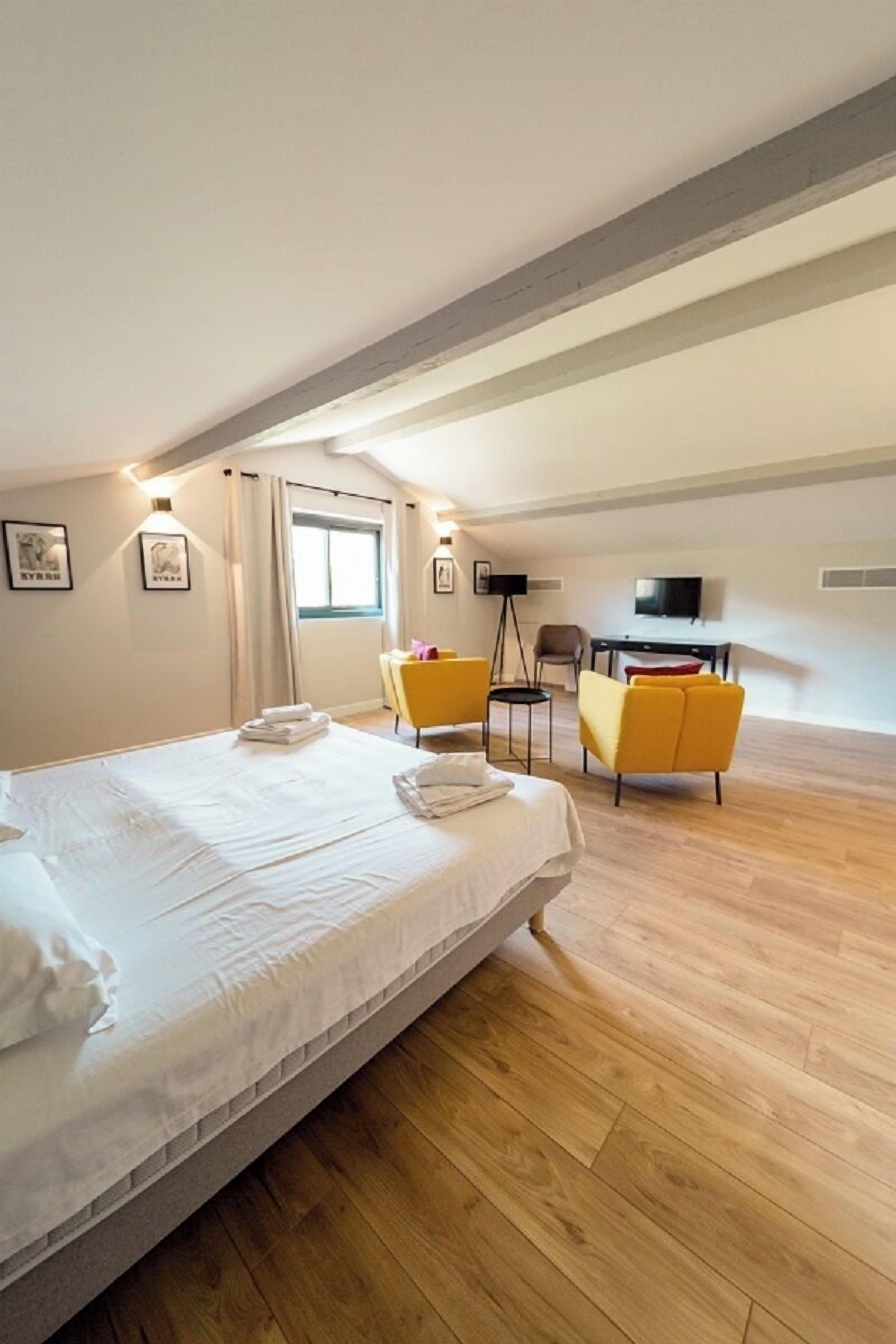 Ein Hotelzimmer mit einem großen Bett, zwei gelben Sesseln, einem Schreibtisch und einem Fernseher.
