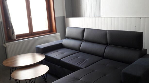 Ett modernt vardagsrum med en svart soffa, två träbord och ett fönster med persienner.