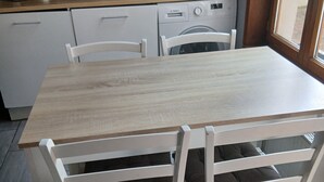 Ett kök med ett träbord och vita stolar, en tvättmaskin från Bosch, en mikrovågsugn och en kaffebryggare.
