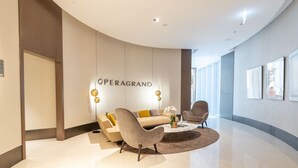 A modern lobby with a curved ceiling, a sofa, two armchairs, a coffee table, and a wall-mounted sign reading "OPERAGRAND". - Vogue, Downtown Opera Grand near Burj Khalifa & Dubai Mall, with Fountain view (Dubai)
