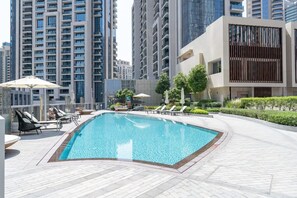 Piscina en la azotea con sillones de descanso y sombrillas, rodeada de edificios modernos.