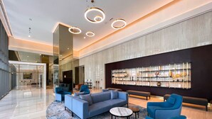 Una hall moderna con un ampio divano grigio, poltrone blu e un tappeto decorato.