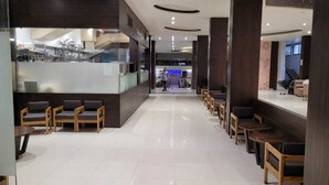 A modern hotel lobby with a reception desk, wooden chairs, and a clean, tiled floor.