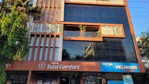 A hotel named 'Tulsi Comfort' with a modern architectural design, featuring large glass windows and a mix of wood and metal elements.