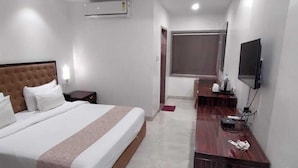 A hotel room with a bed, a desk, a TV, and an air conditioning unit.
