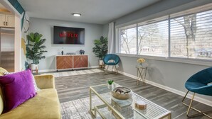 A modern living room with a sofa, coffee table, and a TV mounted on the wall displaying 'NETFLIX'. - Decatur Rocksteady Message for Summer Special (Decatur)