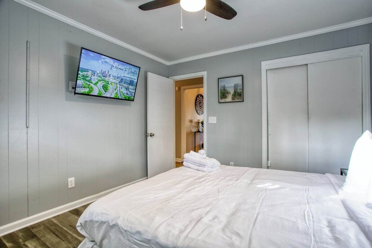 A bedroom with a bed, a ceiling fan, a TV on the wall, and a door leading to another room.
