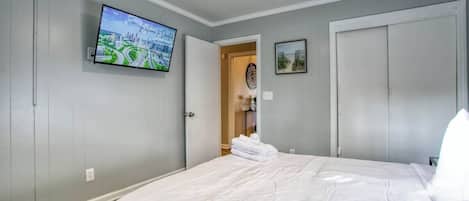 A bedroom with a bed, a ceiling fan, a TV on the wall, and a door leading to another room.