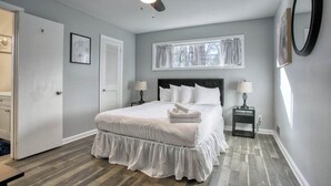 A bedroom with a bed, a ceiling fan, a window with curtains, a bedside table with a lamp, and a door. - Decatur Rocksteady Message for Summer Special (Decatur)