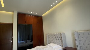 A modern bedroom with two beds, a wooden wardrobe, and a mirror. - Rateel Apartments 3 min walk from Badr Al Sama Hospital  (Salalah)