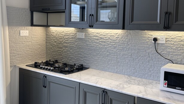 A modern kitchen with grey cabinets, a gas stove, and a microwave. - Rateel Apartments 3 min walk from Badr Al Sama Hospital  (Salalah)