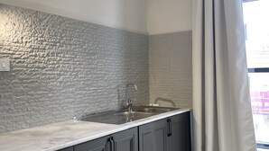 A modern kitchen with a stone backsplash, grey cabinets, and a large window with curtains. - Rateel Apartments 3 min walk from Badr Al Sama Hospital  (Salalah)