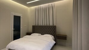 A modern bedroom with a large bed, a headboard, bedside tables, and a door. - Rateel Apartments 3 min walk from Badr Al Sama Hospital  (Salalah)