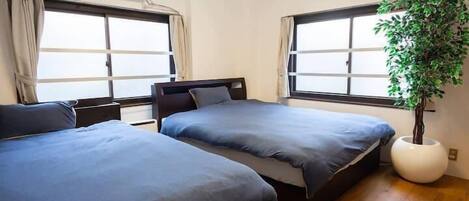 A bedroom with two beds, large windows, a potted plant, and an air conditioning unit.