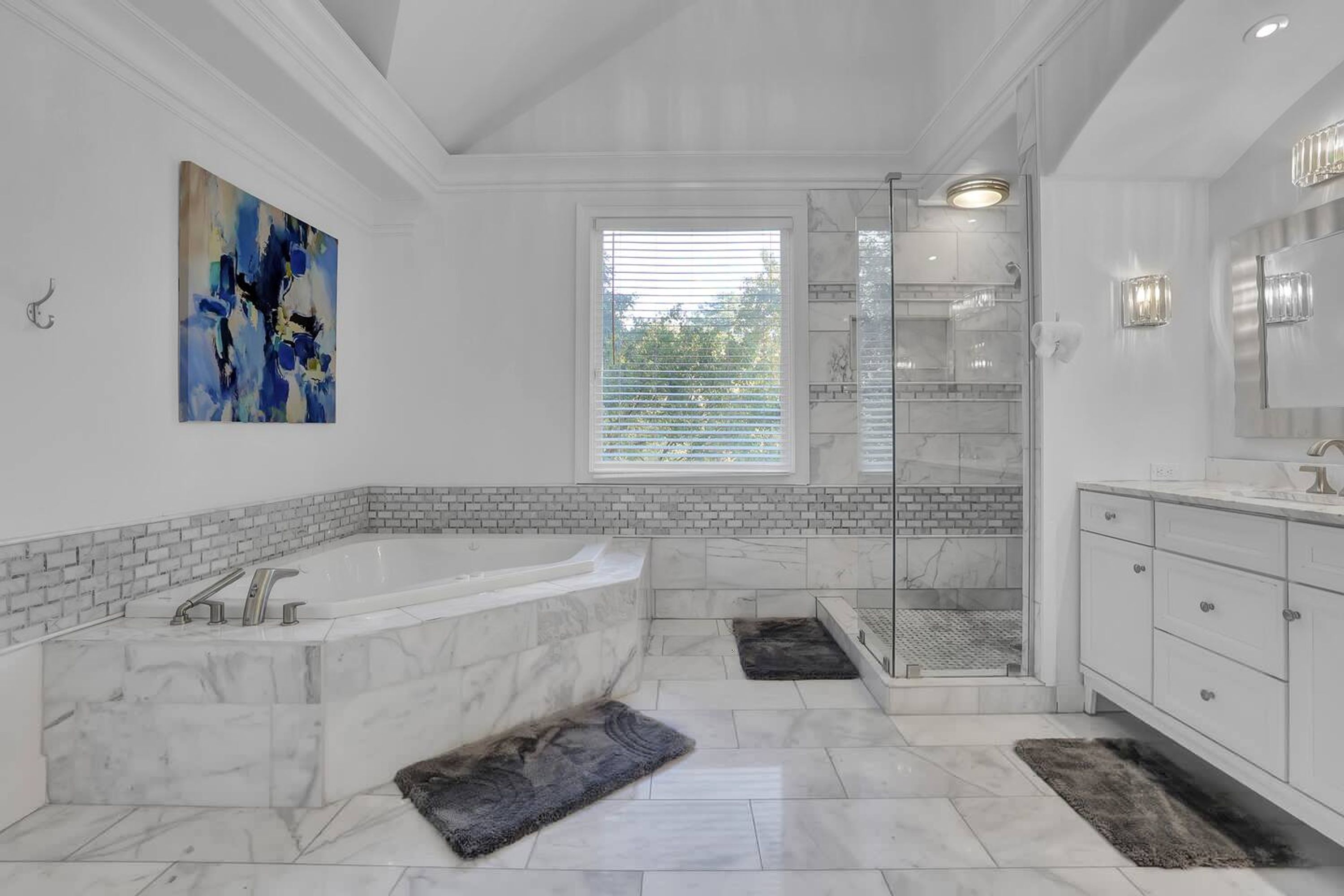 A modern bathroom with a large bathtub, a walk-in shower, and a window with blinds.