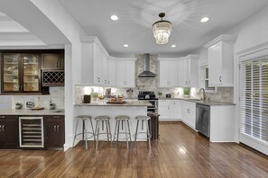 A kitchen with white cabinets, a central island with stools, a stainless steel range hood, and a chandelier. - Buckhead Dream Message Now for Summer Special (Atlanta)