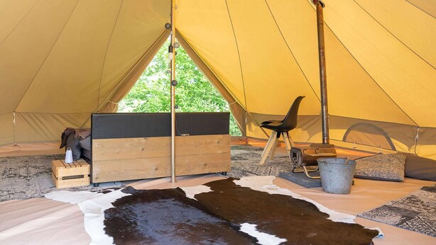 A tent interior with a wooden bench, a chair, a bucket, and a cowhide rug. - Glamping Lodge in Friesland near Nature Reserves (Twijzel)