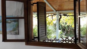 Una ventana abierta con vistas a una pérgola de madera y abundante vegetación.
