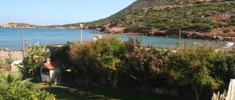 Una propiedad costera con una casa pequeña, un espacio cubierto de césped y vistas al mar y a las colinas.