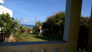 Vista desde un balcón sobre un jardín con una casa pequeña y un cielo azul despejado.