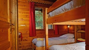 A wooden cabin with bunk beds, a window with red curtains, and a door. - Spacious 8-Bedroom Chalet (Barvaux)