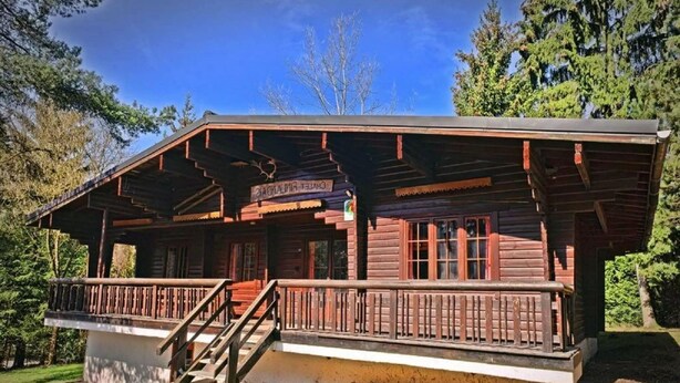 A rustic lodge with a covered porch and a staircase leading to the entrance. - Spacious 8-Bedroom Chalet (Barvaux)