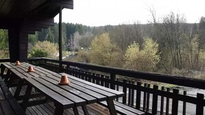 A wooden deck with picnic tables and a railing, overlooking a forested area. - Spacious 8-Bedroom Chalet (Barvaux)