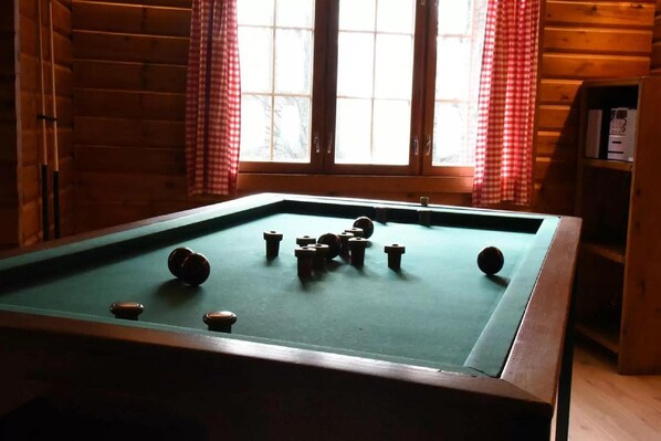 Una mesa de billar en una habitación con paredes de madera y un ventanal con cortinas rojas.