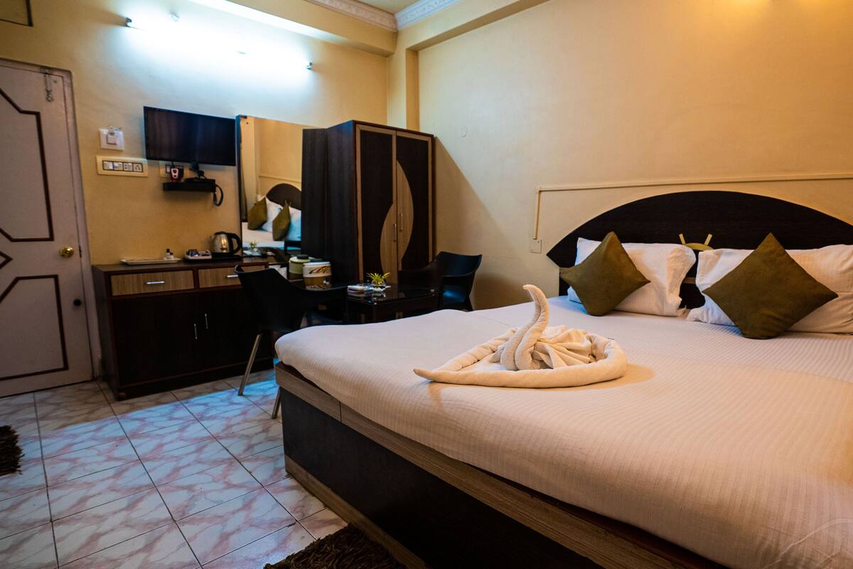 Habitación de hotel con cama, escritorio, silla, armario y televisor.