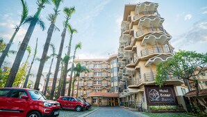 Un hôtel à plusieurs étages, doté de balcons, de palmiers et d’une aire de stationnement.