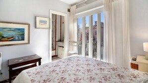 Une chambre à coucher avec un lit, un bureau, une chaise, une fenêtre avec des rideaux et un tableau au mur.