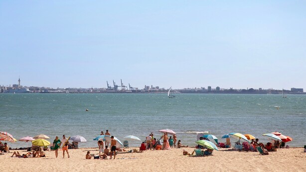 Une plage avec des gens, des parasols et des bateaux en arrière-plan.