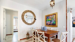 Un coin repas avec une table en bois, des chaises blanches, un miroir décoratif et un tableau coloré accroché au mur.