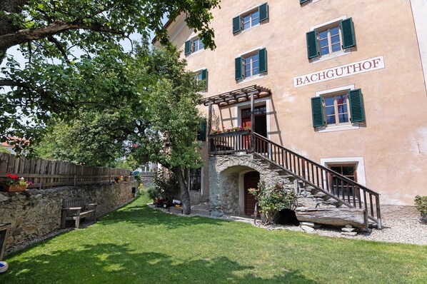 A building with a stone staircase, a wooden deck, and a name 'BACHGUTHOF' on the facade.