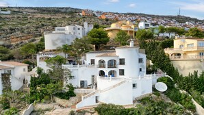 A white villa with a balcony, surrounded by greenery and a hillside town in the background. - Villa 'Costa Blanca' with Sea View, Wi-Fi and Air Conditioning (Benitachell)
