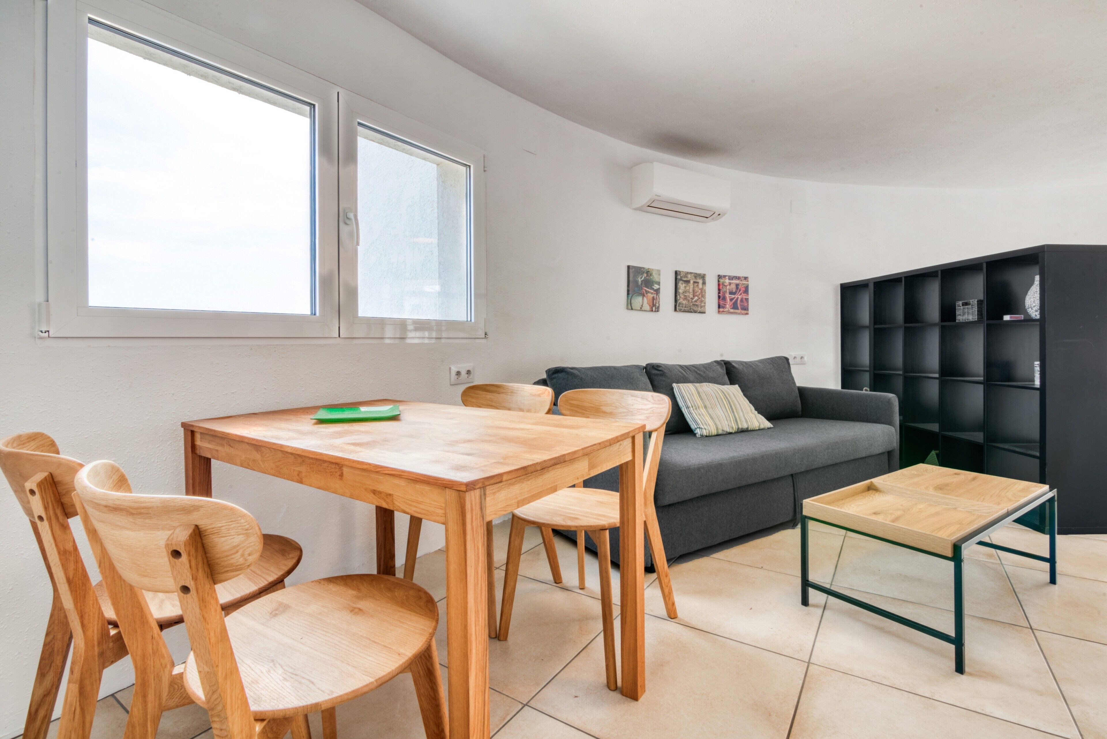 Una sala de estar moderna con una mesa de comedor de madera, sillas, un sofá y una estantería.