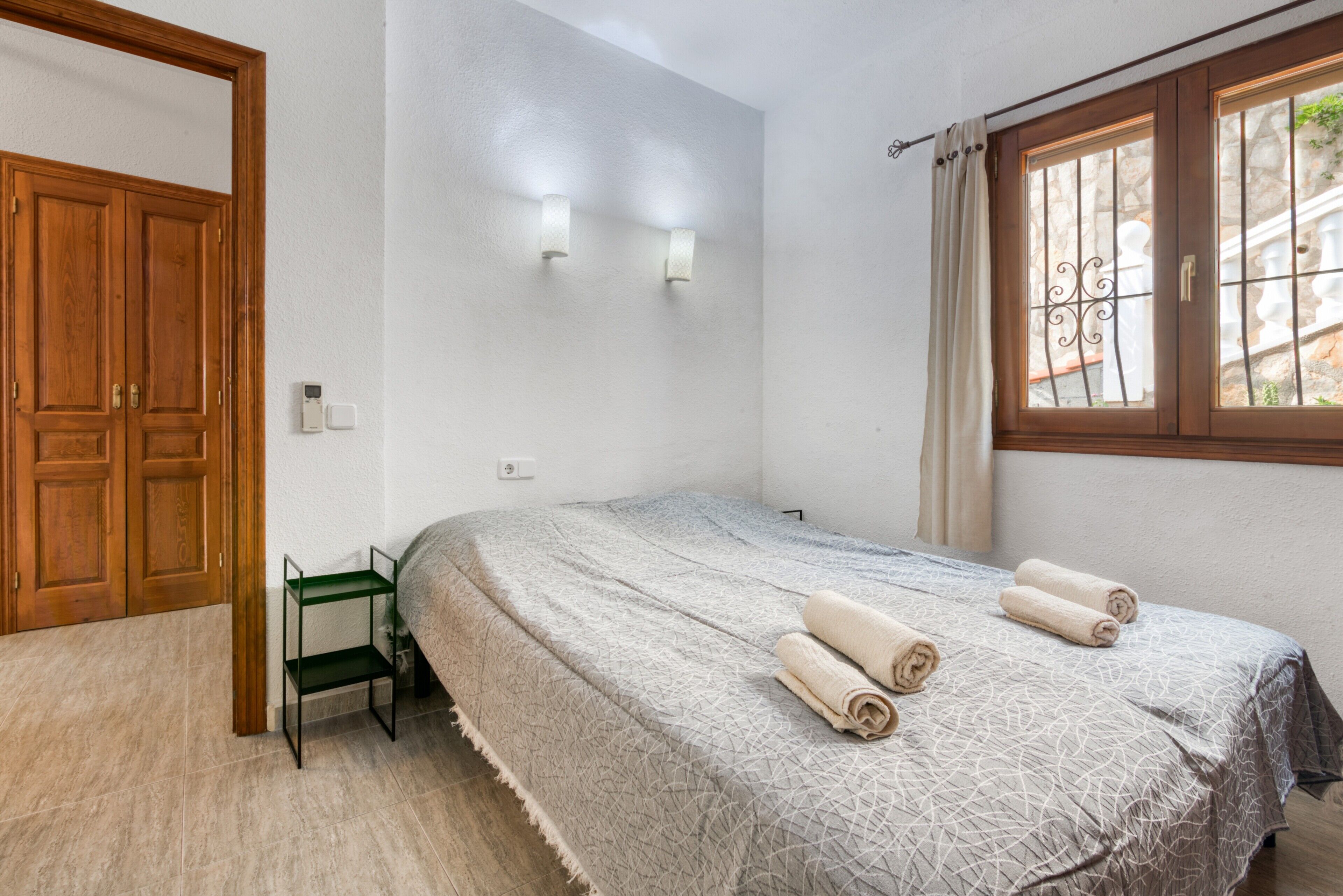 Un dormitorio con una cama, una puerta de madera, una ventana con barrotes y un estante de metal verde.