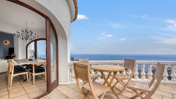 A balcony with a dining set and chairs, a view of the sea, and a building with a white exterior and wooden accents. - Villa 'Costa Blanca' with Sea View, Wi-Fi and Air Conditioning (Benitachell)