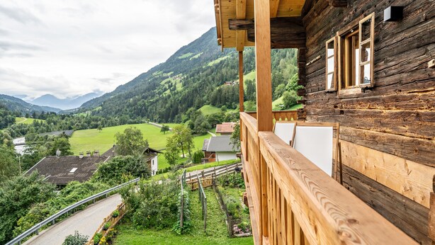 A wooden cabin with a balcony overlooking a valley and mountains.