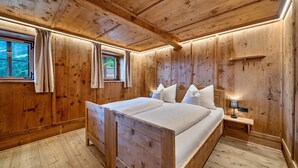A wooden-paneled bedroom with a bed, curtains, a nightstand, and a window.