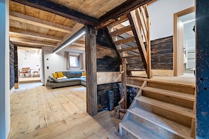 A rustic interior with a wooden staircase, a sofa with cushions, and a fireplace.