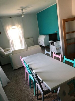 Una habitación con un sofá blanco, una mesita, un ventilador de techo, una ventana con cortinas y una pared verde azulado.