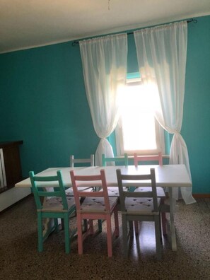 Un comedor con mesa y sillas, una ventana con cortinas y paredes color aguamarina.