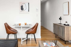 Una sala de estar moderna con una mesa blanca, dos sillones de cuero marrón, un aparador de madera y una lámpara de pie negra.