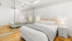 Un dormitorio moderno con una cama grande, mesitas de noche, un espejo y un ventilador de techo.