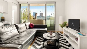 A modern living room with a black leather sofa, a round coffee table, and a TV on a white stand.