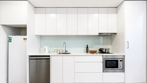 A modern kitchen with white cabinets, a dishwasher, a sink, a microwave, and a stove.