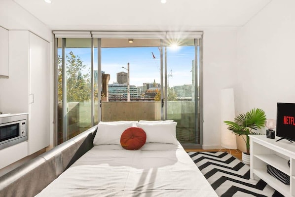 Enjoy a city view from the comfort of a spacious bed, with a flat-screen TV and a touch of greenery nearby.